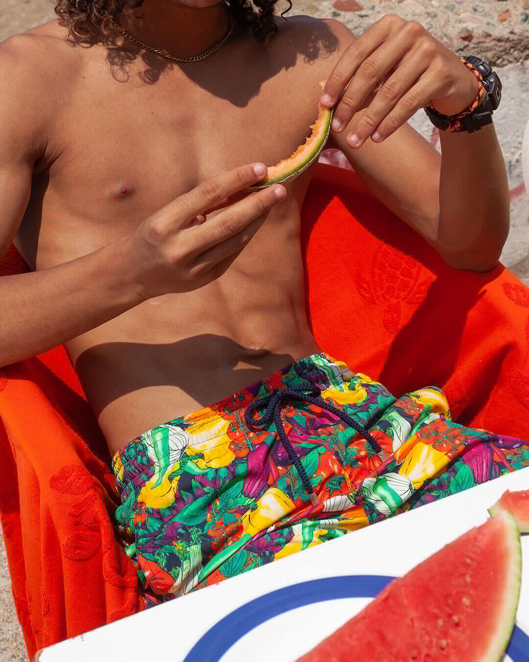 Man wearing a swim short eating a watermelon